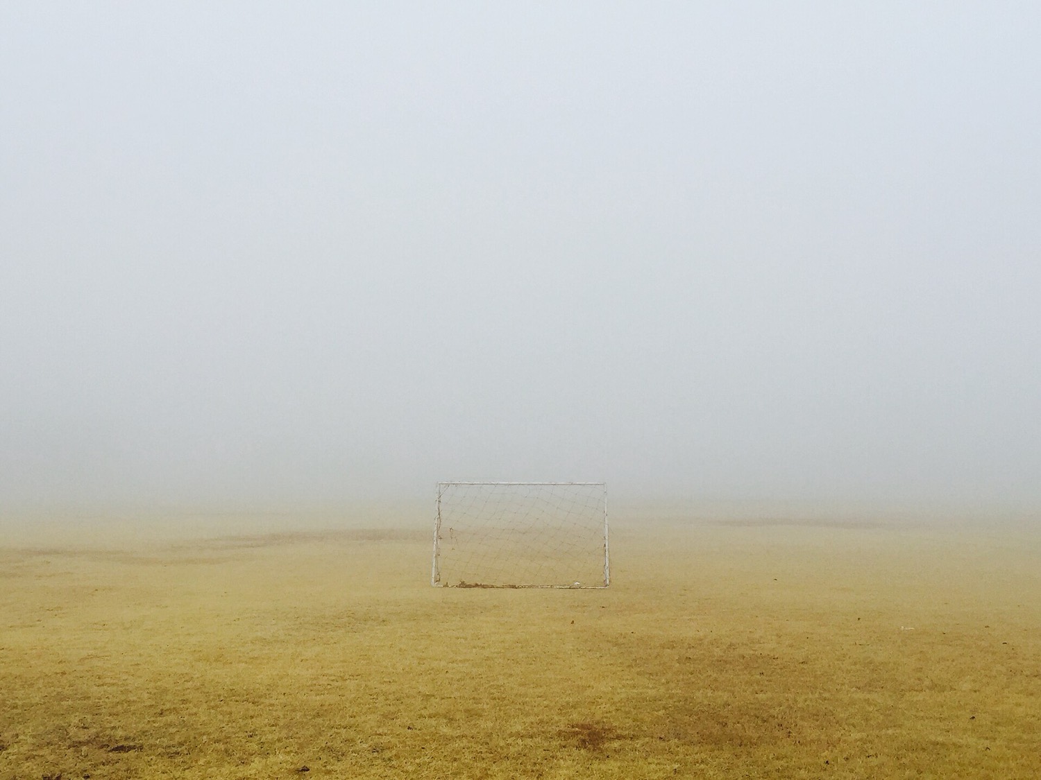 霧のグラウンドの中央に立つサッカーゴール